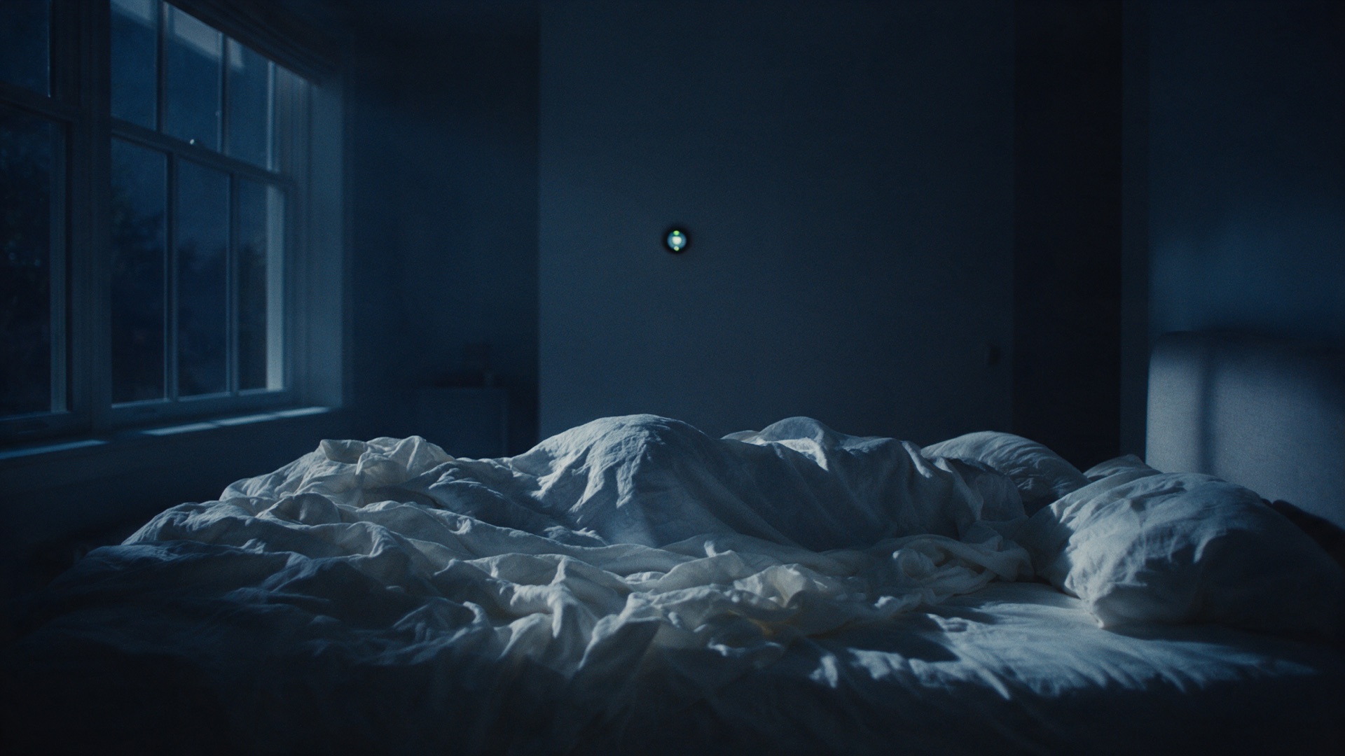 A dark bedroom at night, a thermostat glowing softly on the wall